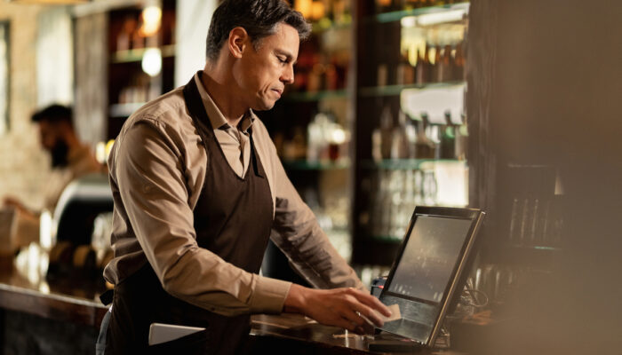 Mid adult barista checking orders at cash register while working in a pub.